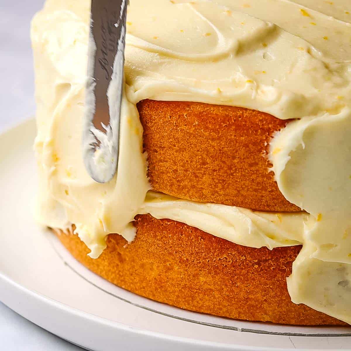 frosting the sides of the orange layer cake with cream cheese frosting using an offset spatula