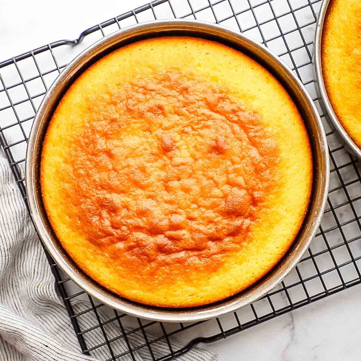 baked orange cake in a cake pan placed on a wire rack
