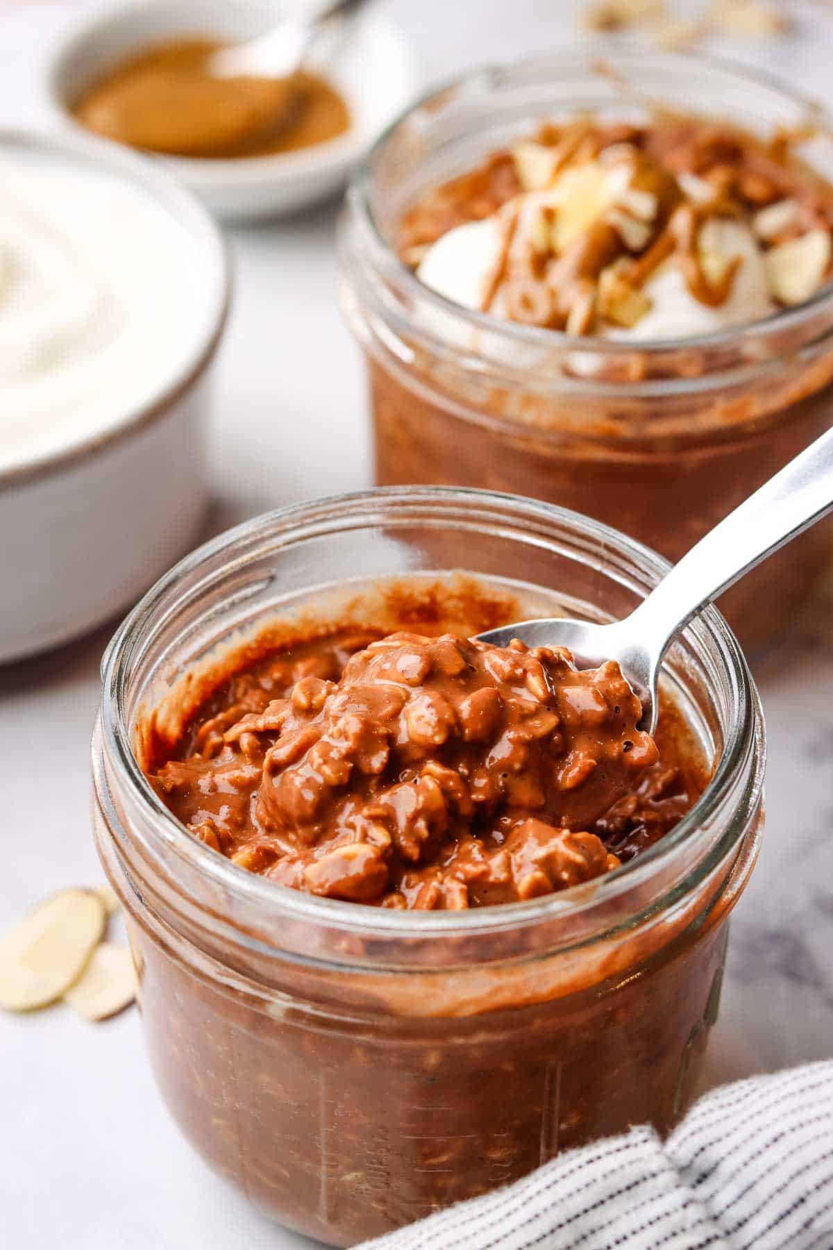 picking up a spoonful of overnight oats from a mason jar