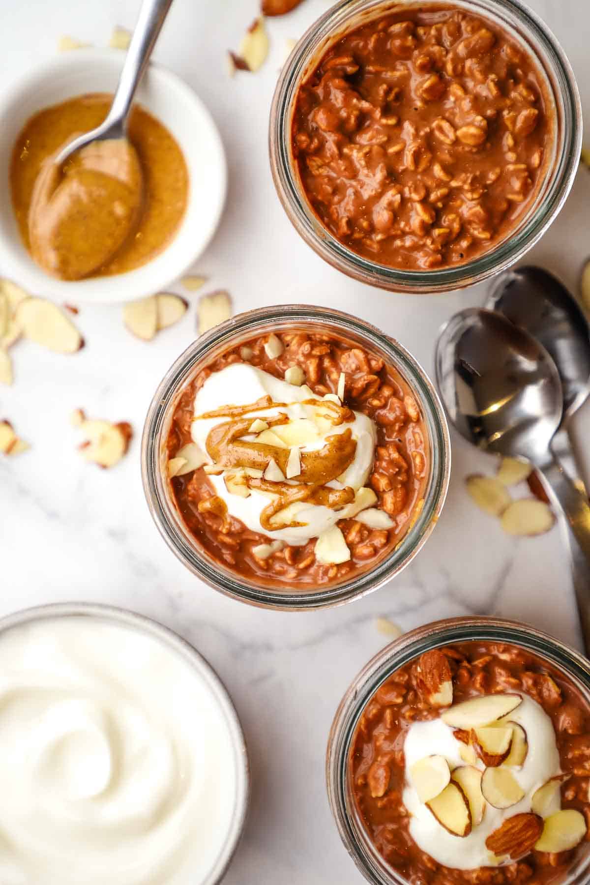 overhead view of mason jars of chocolate overnight oats topped with yogurt and almonds.