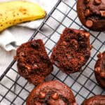 Chocolate banana muffins on a cooling with a muffin split in two to show the inside.