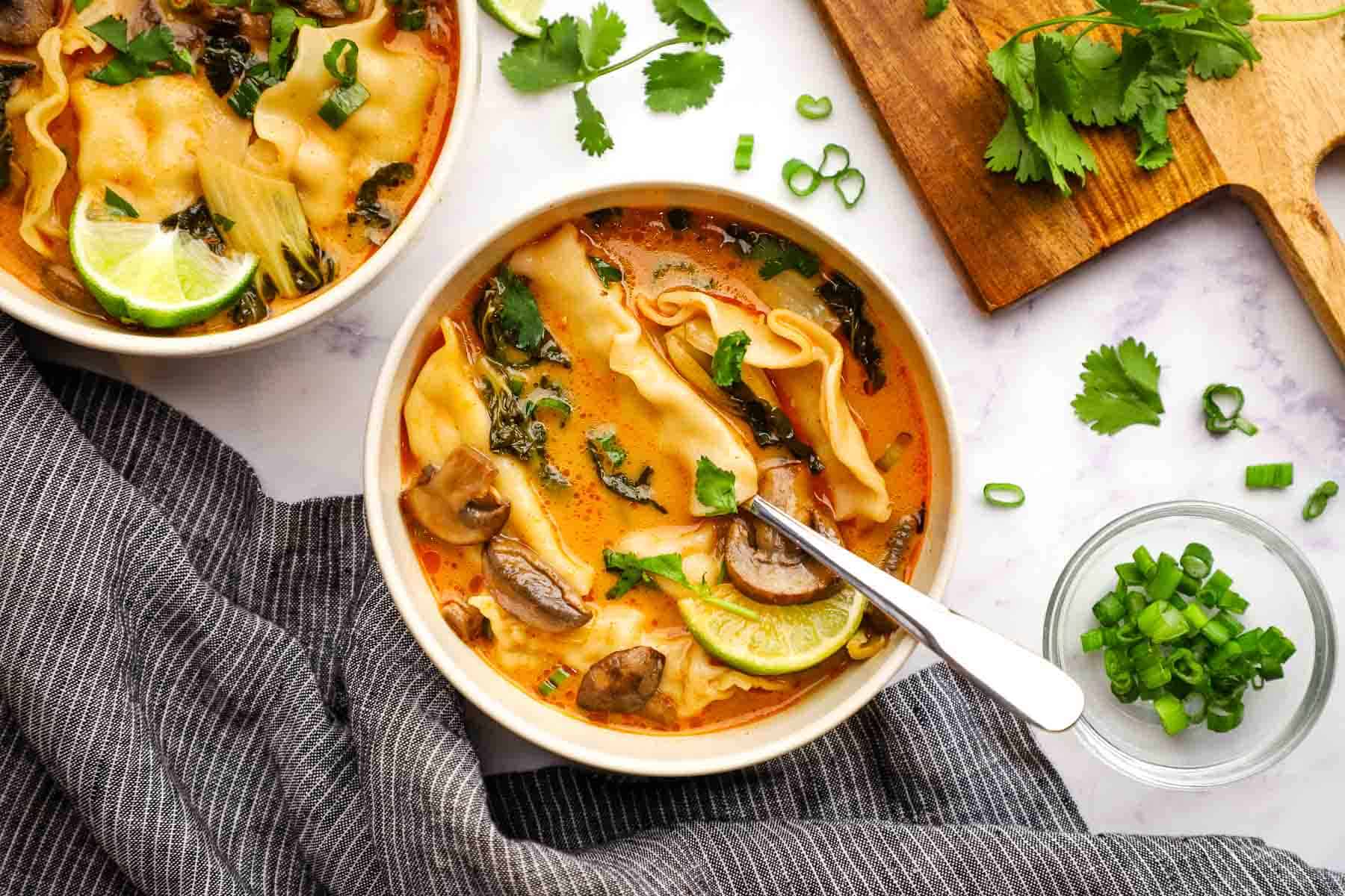 A bowl of red curry dumpling soup with a spoon in it.