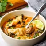 A bowl of red curry dumpling soup with a spoon in it.