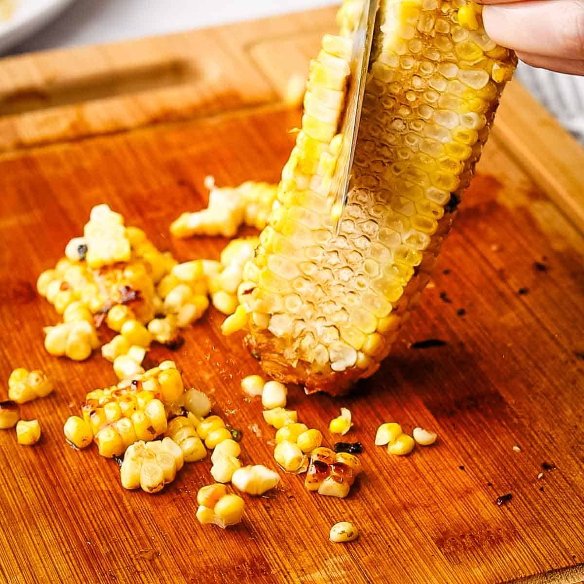 running down a knife lengthwise on a corn cob to cut off the corn kernels