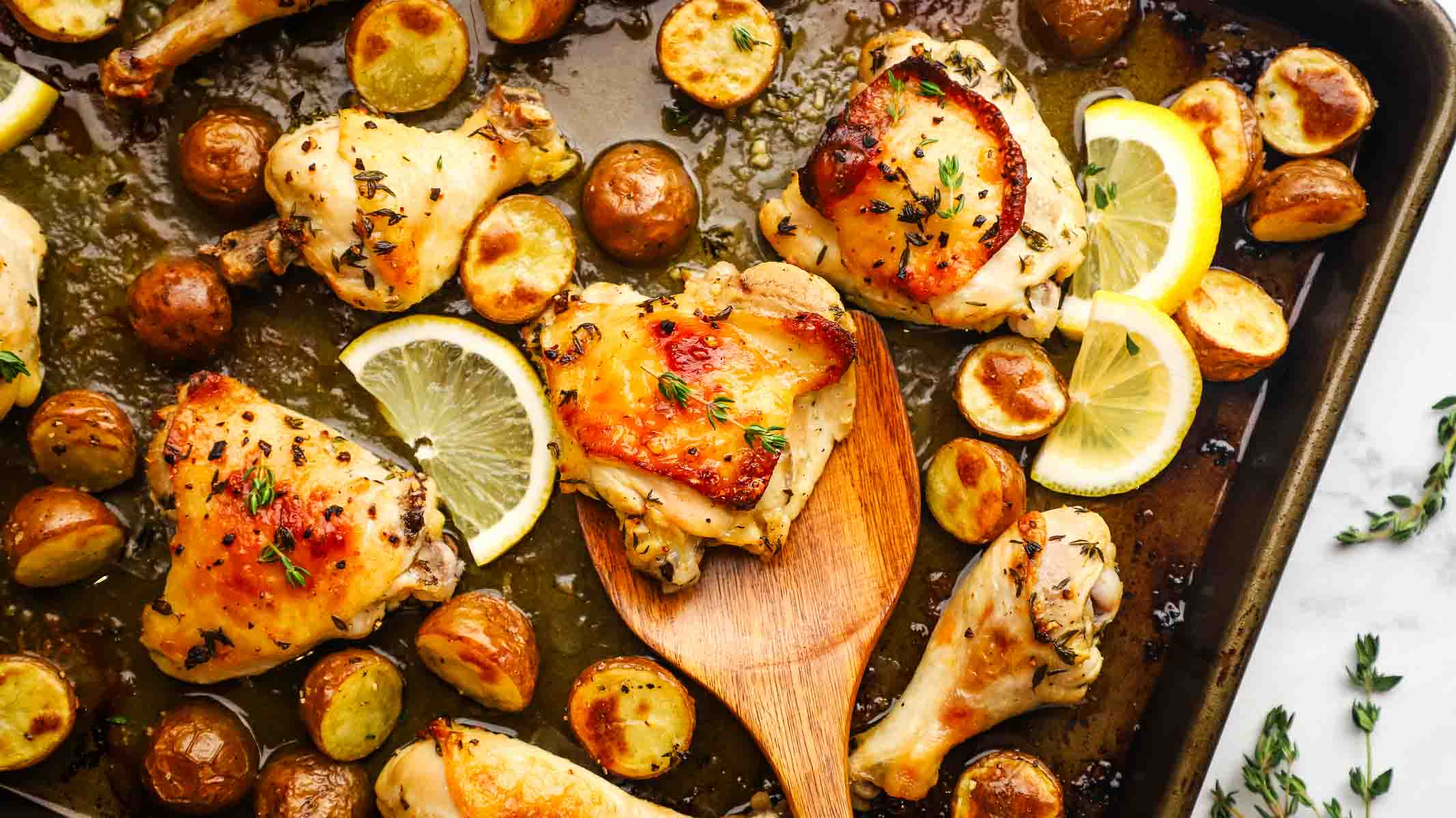 Baked chicken parts on a sheet pan with potatoes, garnished with lemon slices.