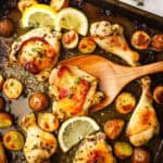 Roasted chicken parts and potatoes on a sheet pan with a wooden spatula.