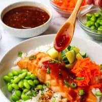 A spoon drizzling glaze over a salmon filet on a bed of rice with fresh vegetables.