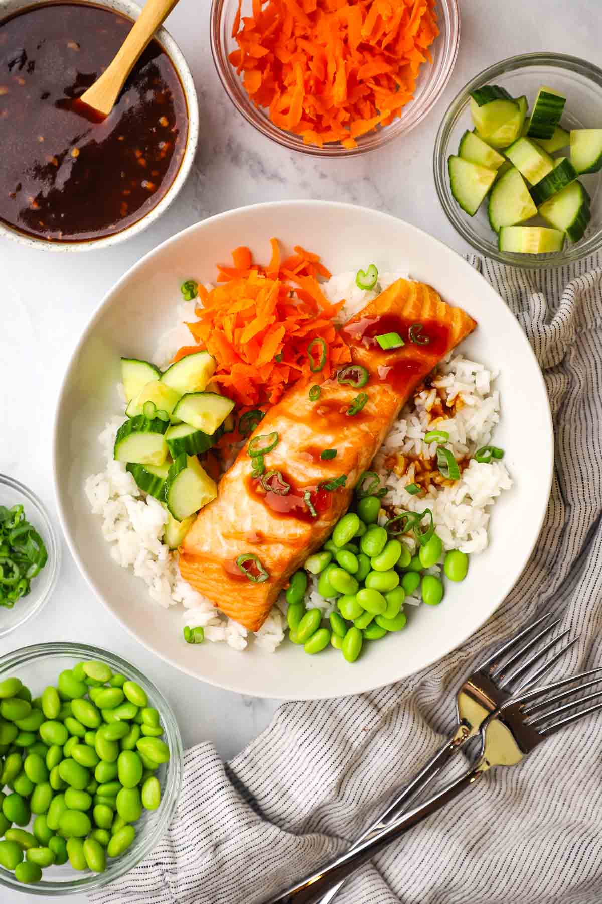 A salmon filet over rice with edamame, carrots, and cucumbers.