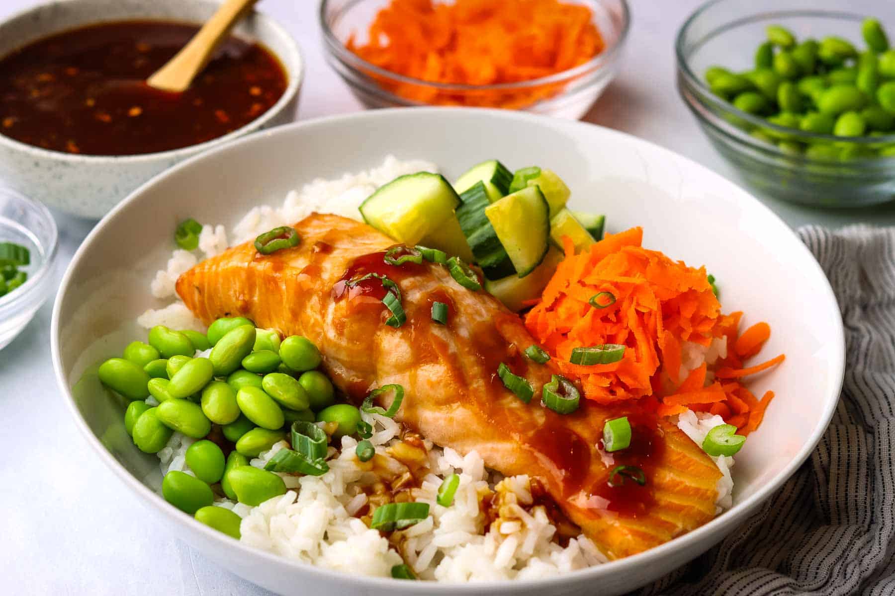 A salmon filet over rice with edamame, carrots, and cucumbers.