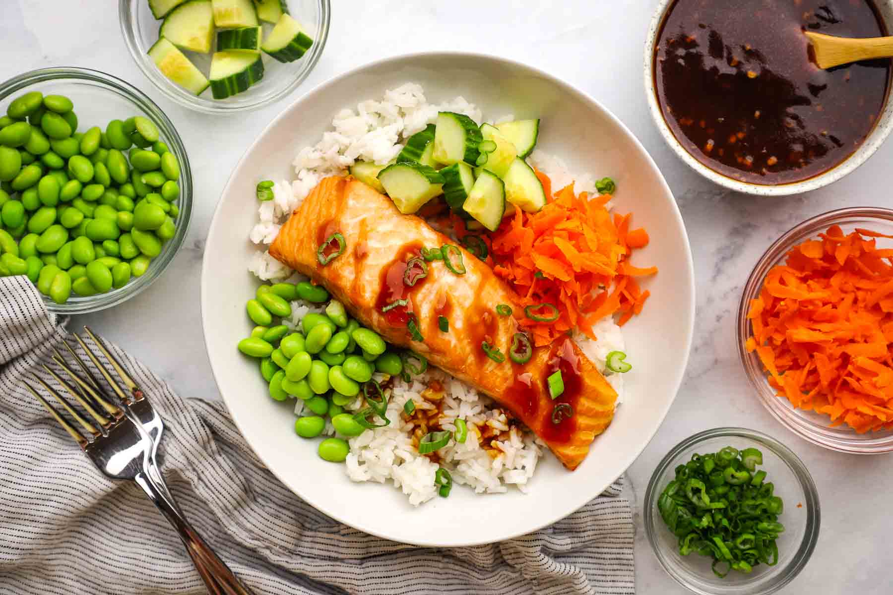 A teriyaki salmon bowl with bowls of toppings surrounding it.