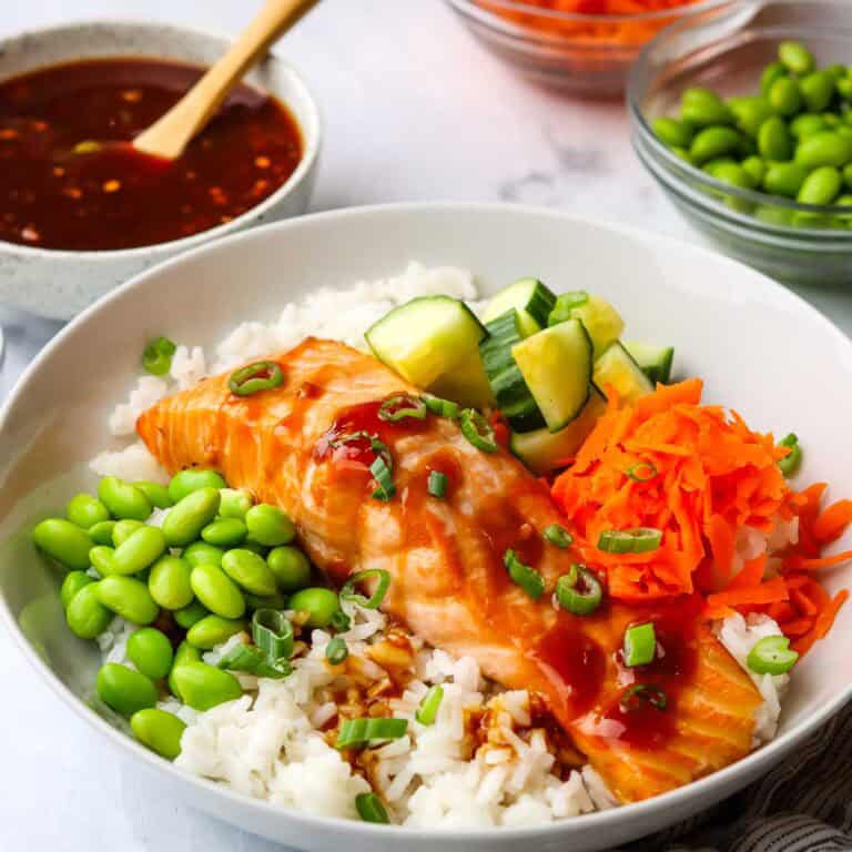 A salmon filet over rice with edamame, carrots, and cucumbers.