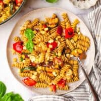 A plate of balsamic pasta salad garnished with basil with a fork in it.