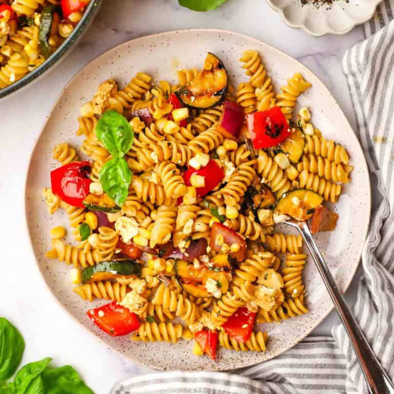 A plate of balsamic pasta salad garnished with basil with a fork in it.