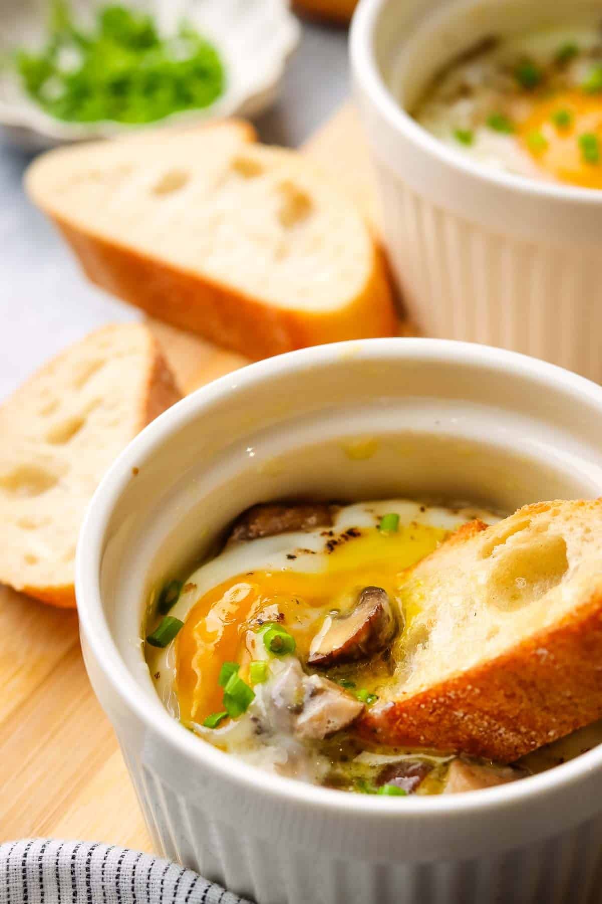 A ramekin with a baked egg in it with a baguette slice dipped into the yolk.