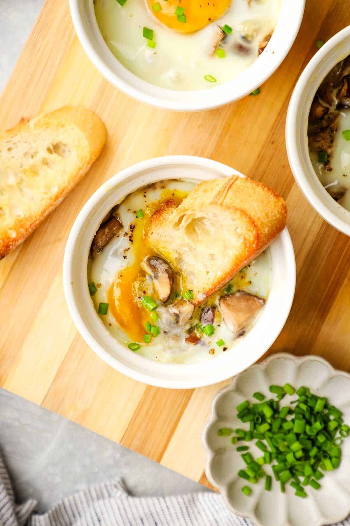 A ramekin with a baked egg in it with a baguette slice dipped into the yolk.