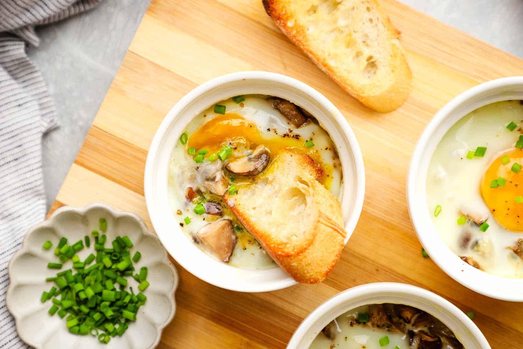 A baked egg in a ramekin with a slice of baguette.
