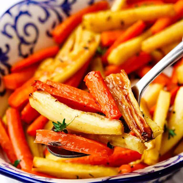 Honey roasted carrots and parsnips in a serving bowl with a spoon.