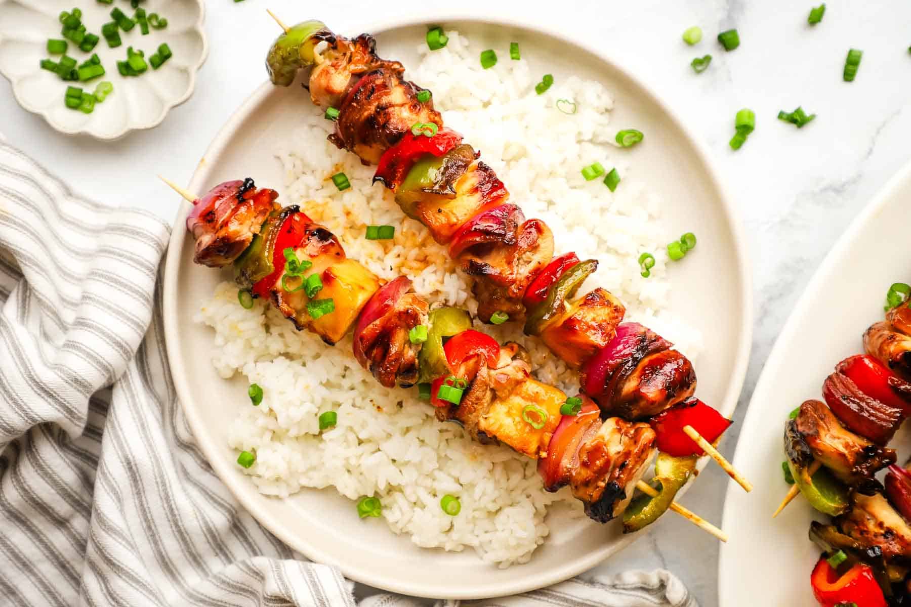 A plate of teriyaki chicken and vegetable skewers served over rice.