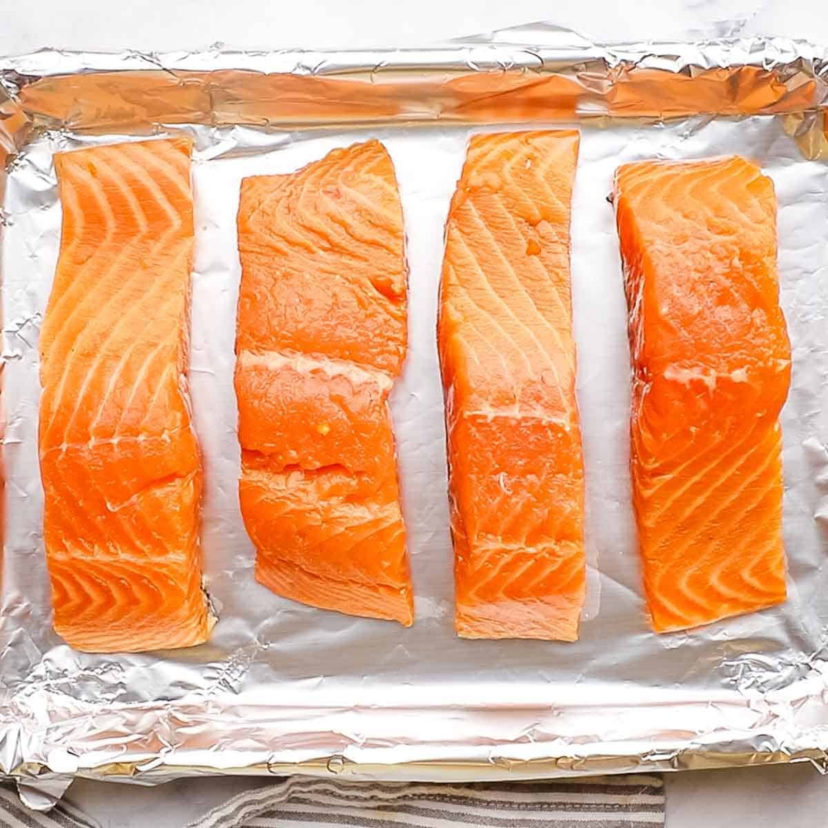 Four salmon fillets on a foil-lined baking sheet.