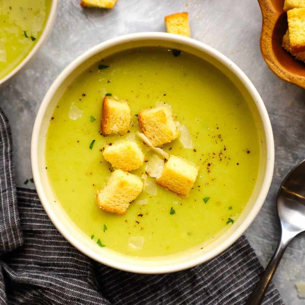 A bowl of asparagus potato soup topped with croutons and parsley.