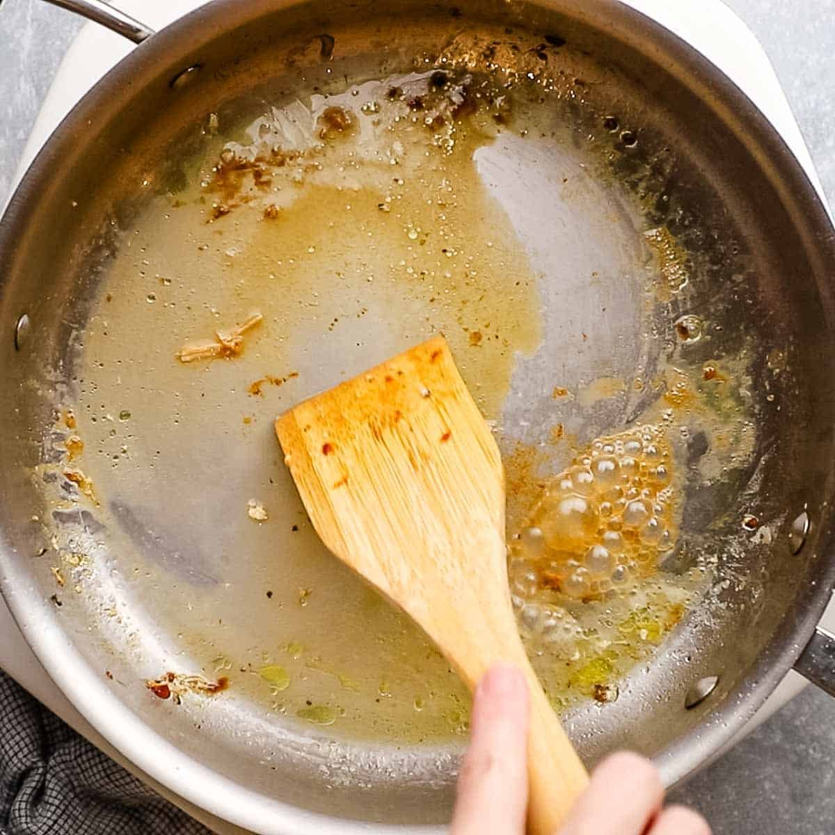 scraping off the brown bit from the skillet with a wooden spoon and some water