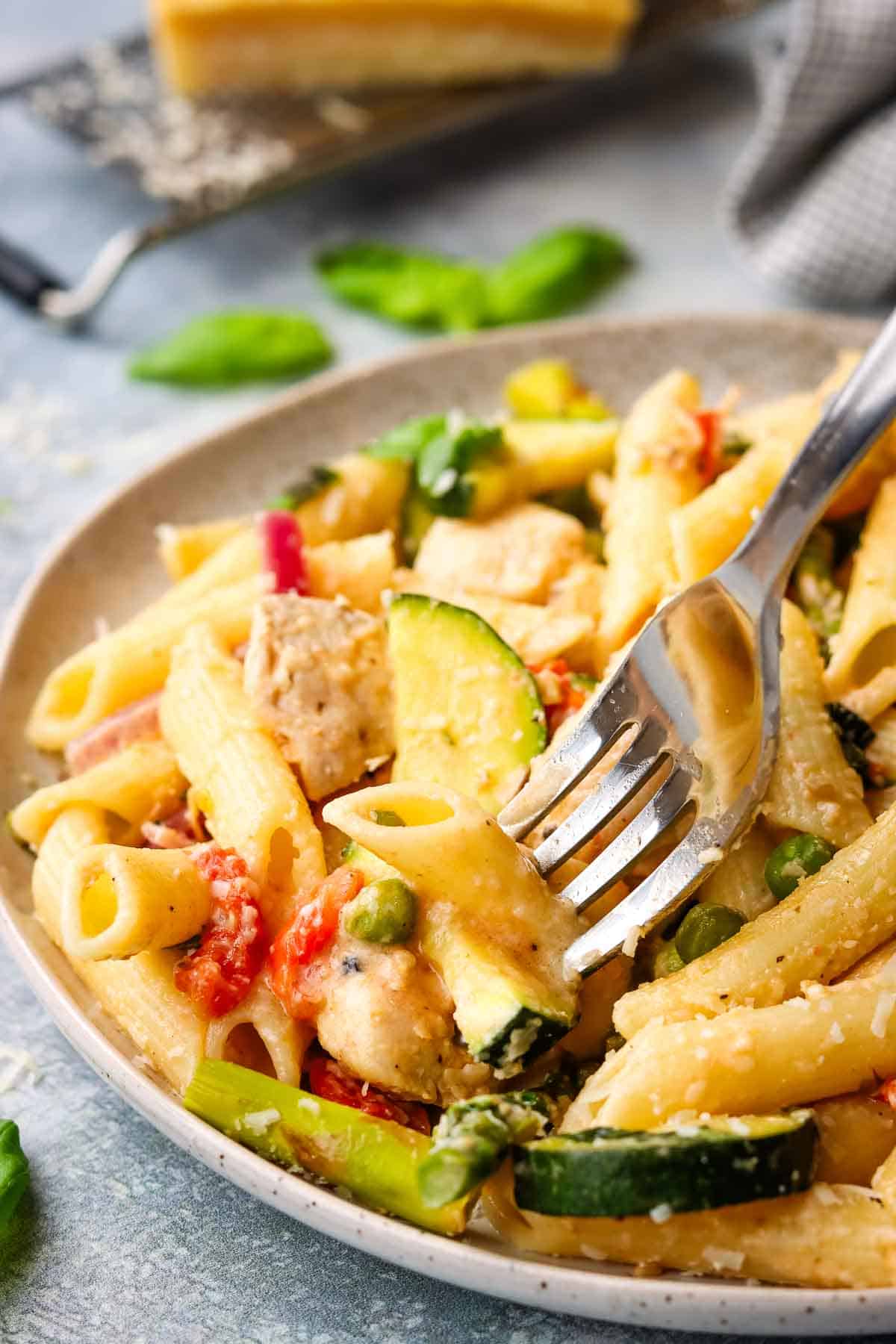 A plate of pasta primavera with a fork in it.