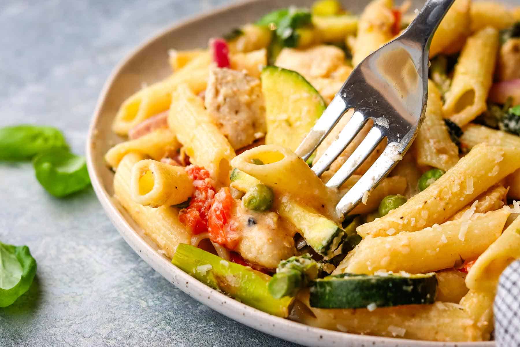 A plate of pasta primavera with a fork in it.