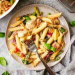 A plate of pasta primavera with a fork in it.