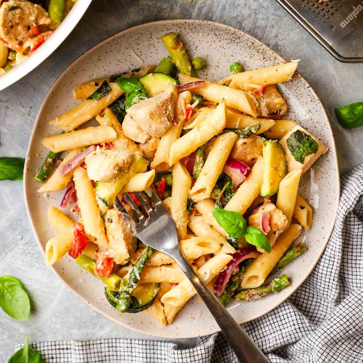 A plate of pasta primavera with a fork in it.