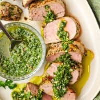 A plate of sliced pork tenderloin with chimichurri on top.