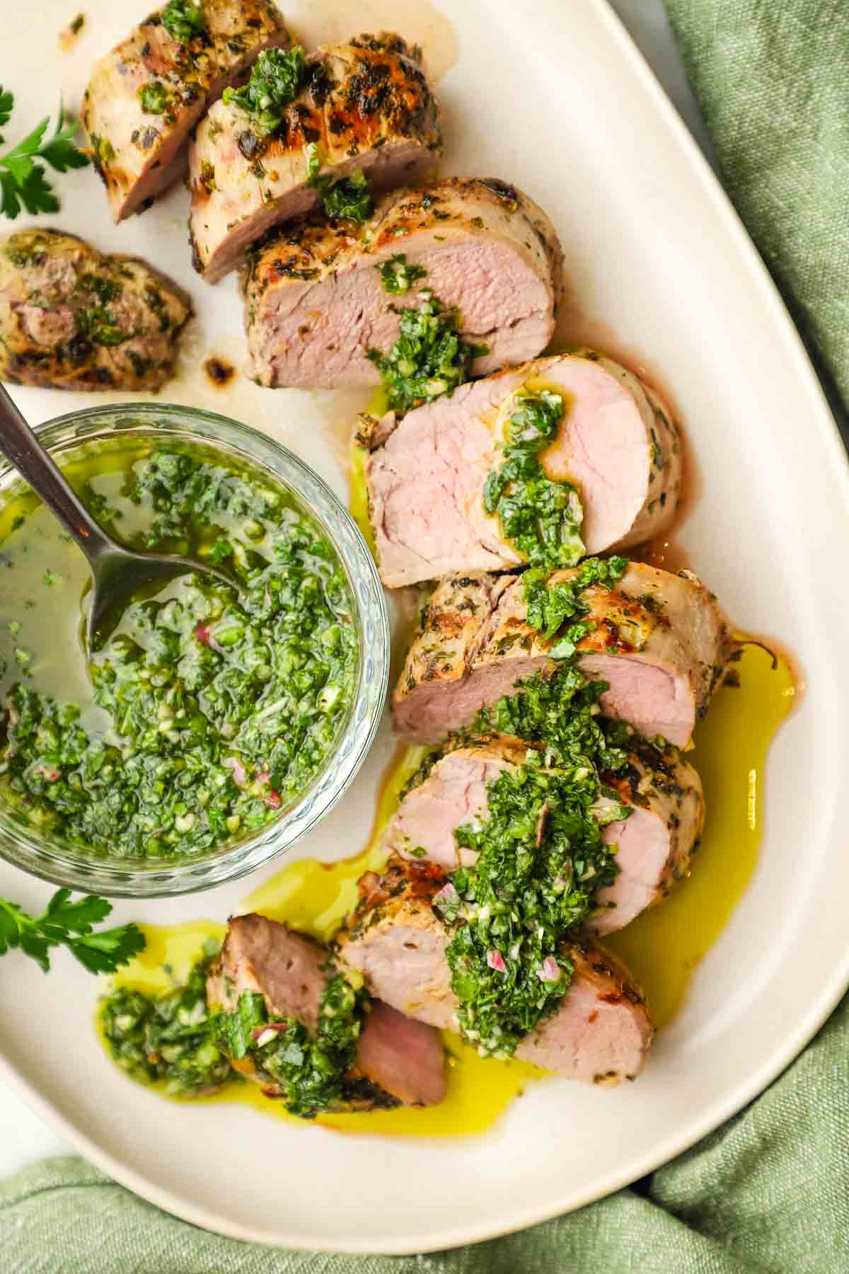 A plate of sliced pork tenderloin with chimichurri on top.