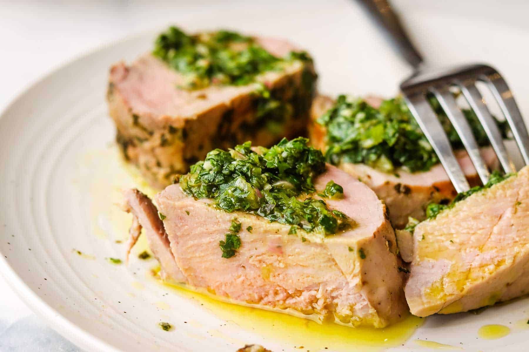 A plate of sliced pork tenderloin with chimichurri on top.