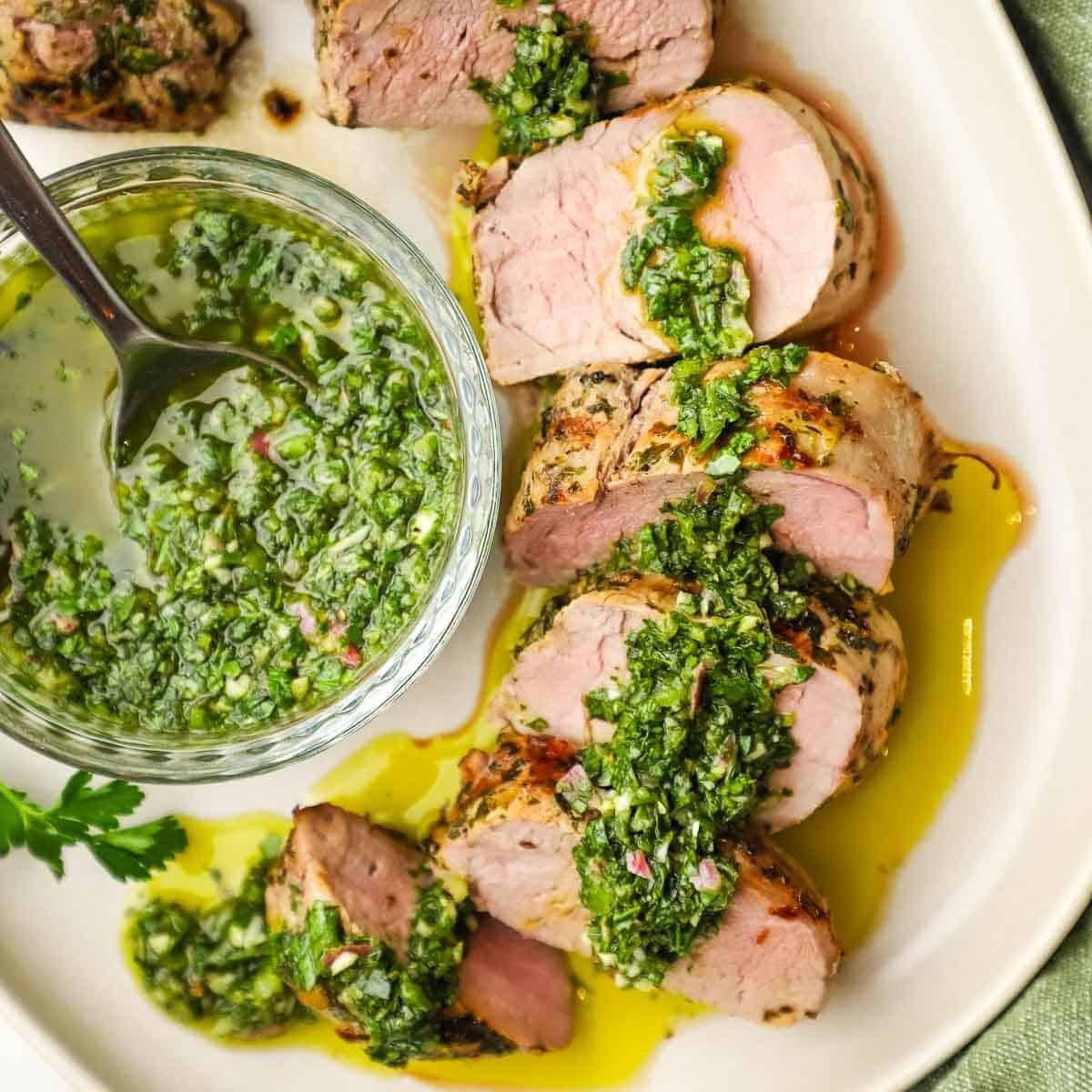A plate of sliced pork tenderloin with chimichurri on top.
