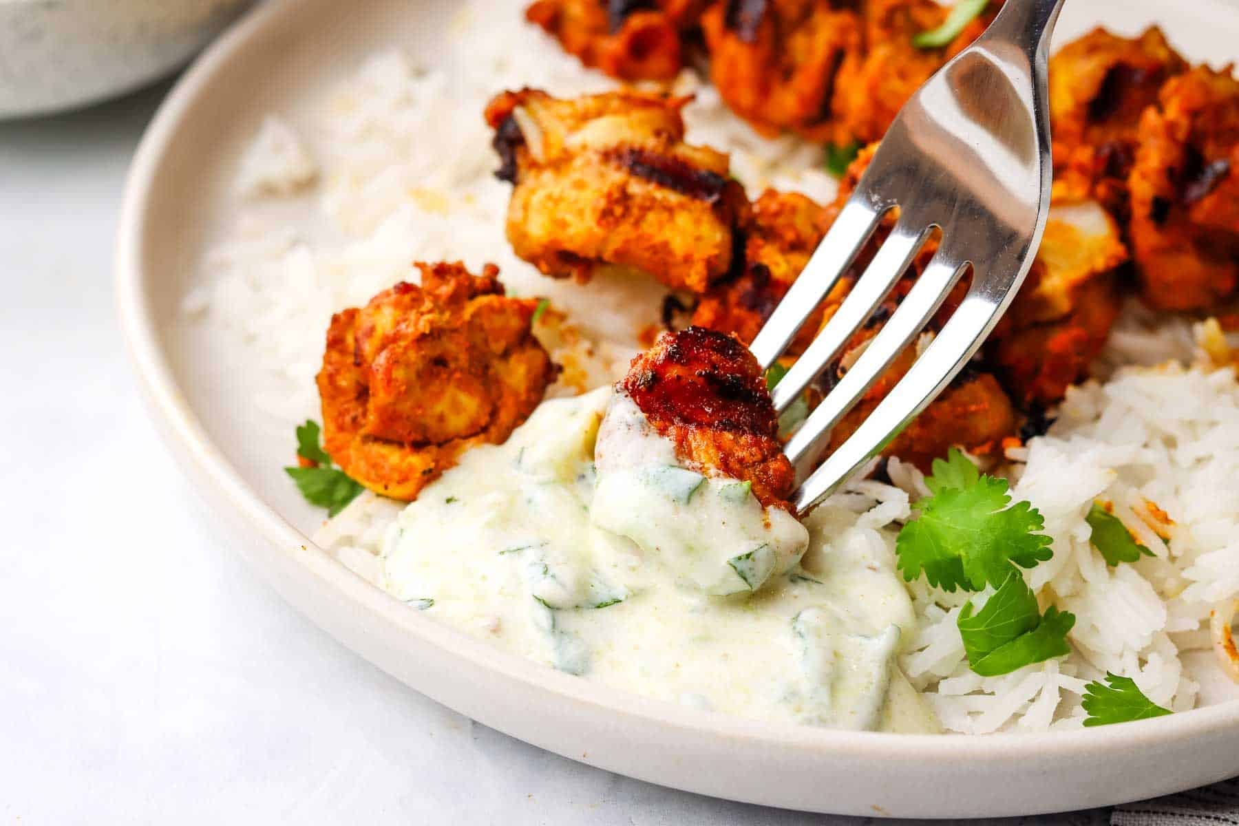 take a bite of chicken from a skewer with a fork