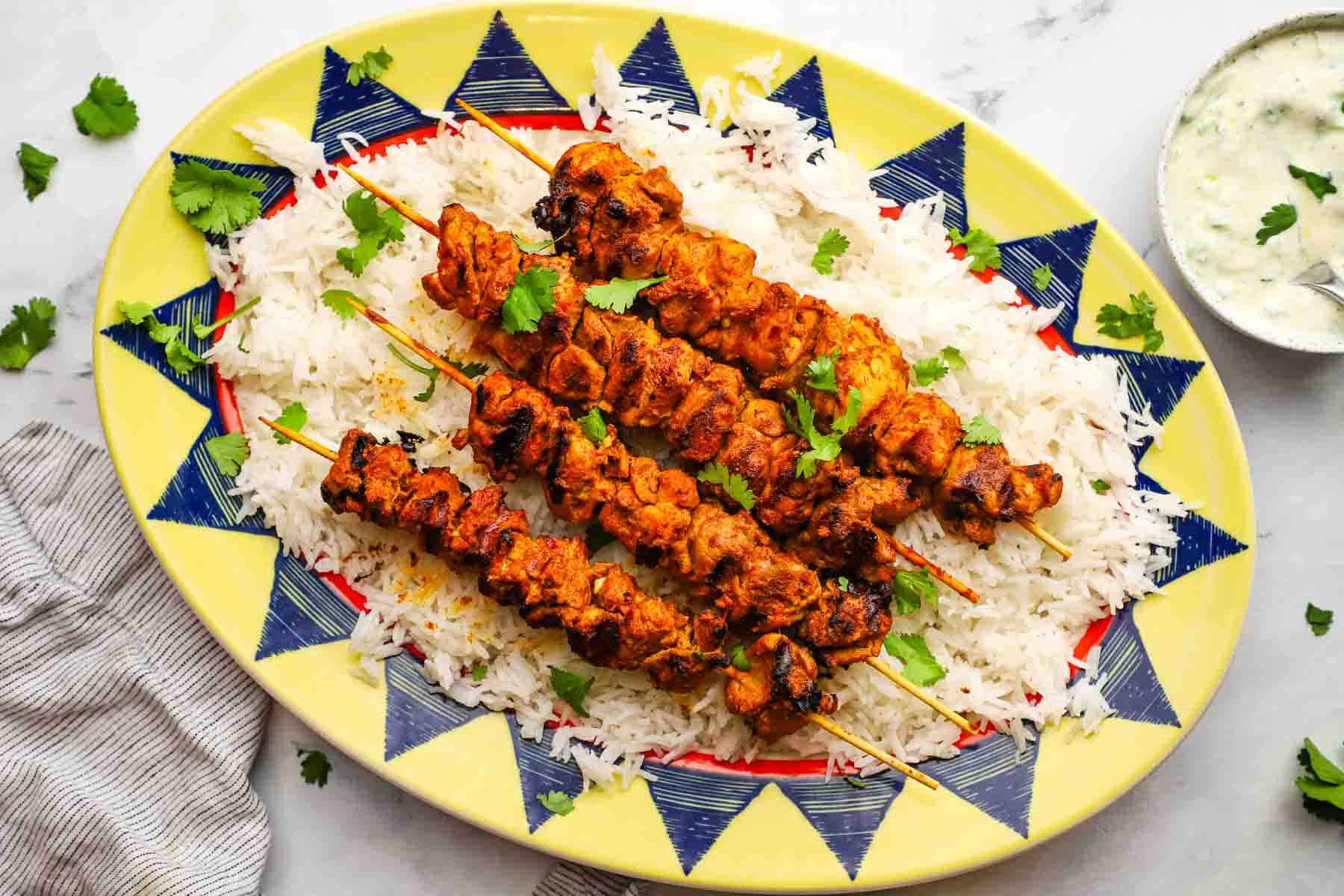 A serving platter of tandoori chicken skewers on a bed of rice.