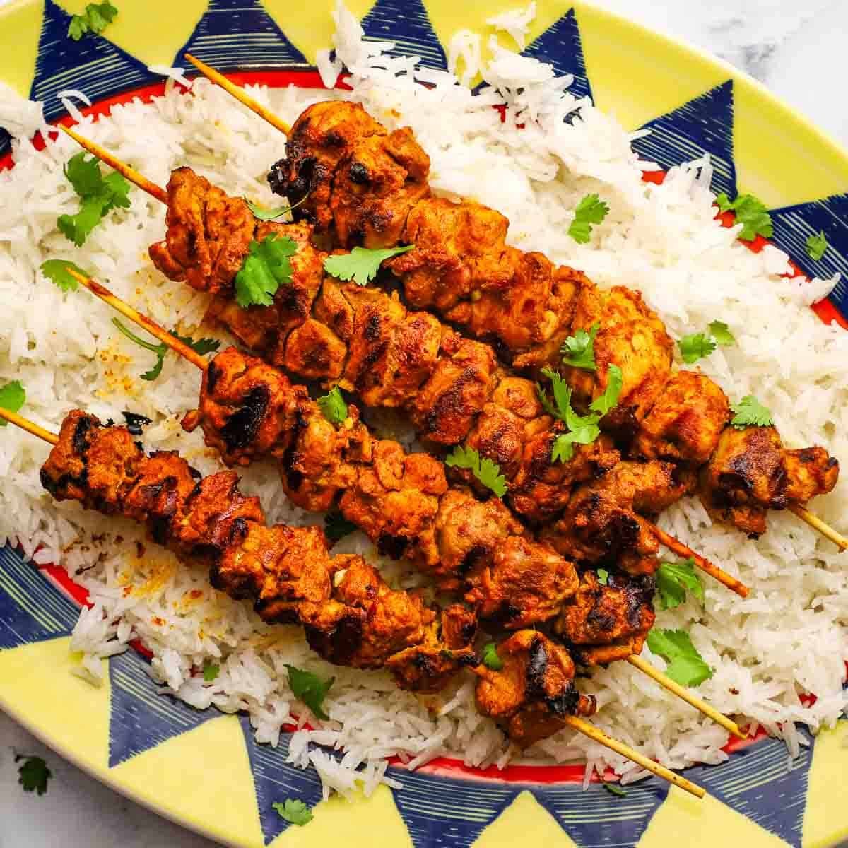 A serving platter of tandoori chicken skewers on a bed of rice.