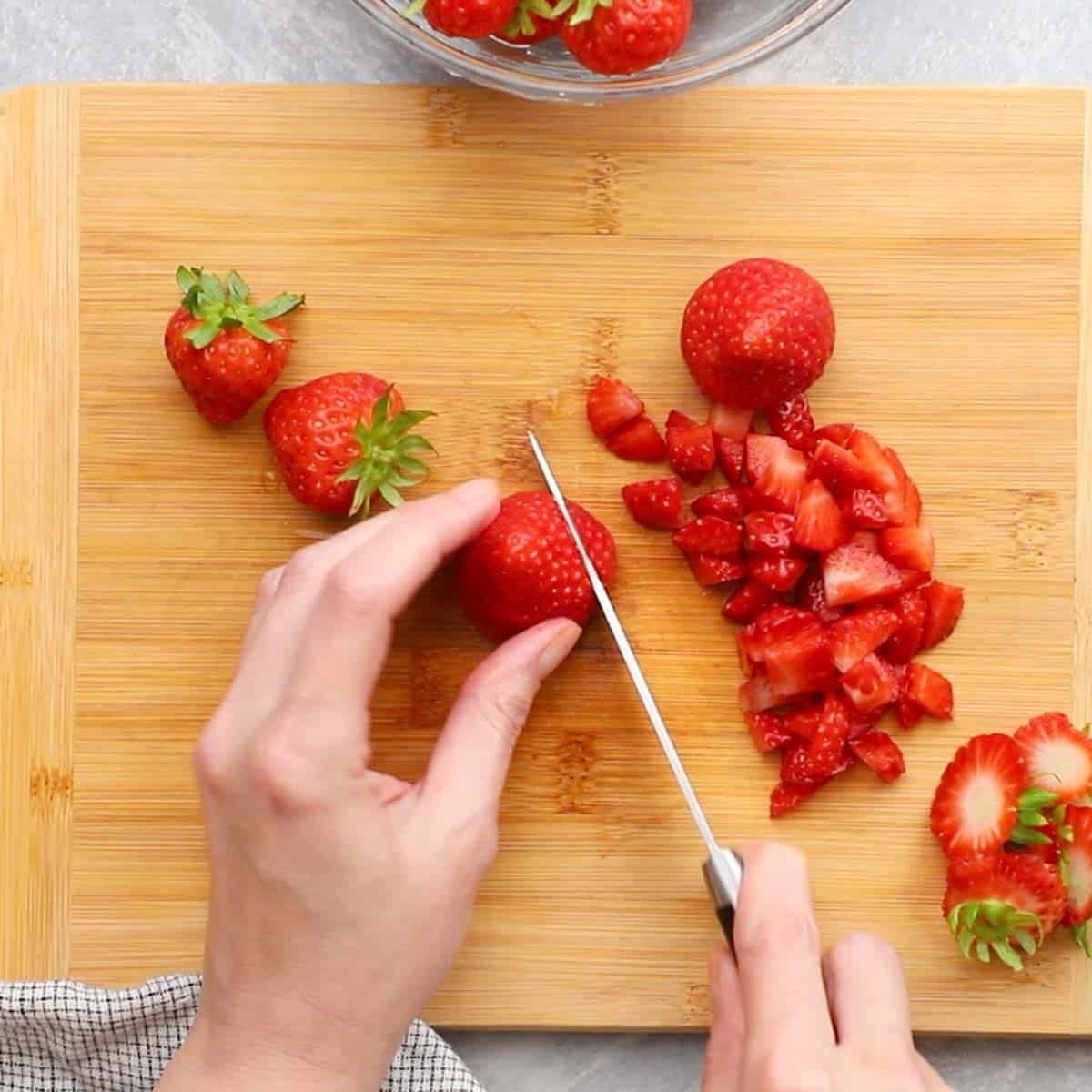 a hand chopping up strawberries on a cutting board