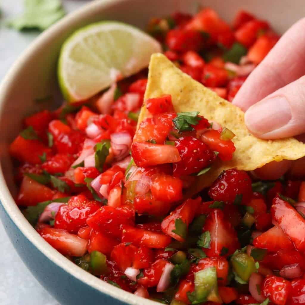 a hand scooping up strawberry salsa with a chip.