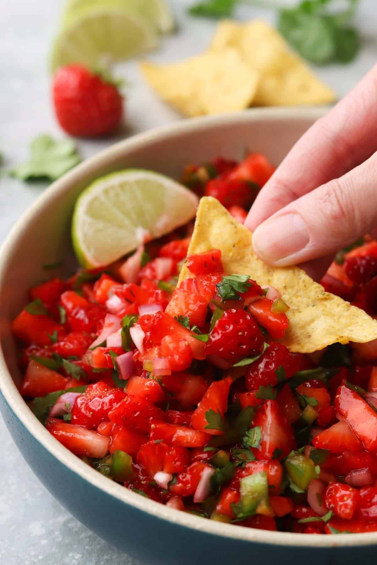 a hand scooping up strawberry salsa with a tortilla chip.