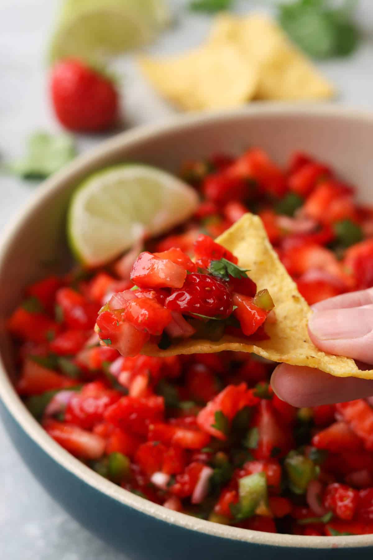 a hand using a tortilla chip to hold a scoop of strawberry salsa