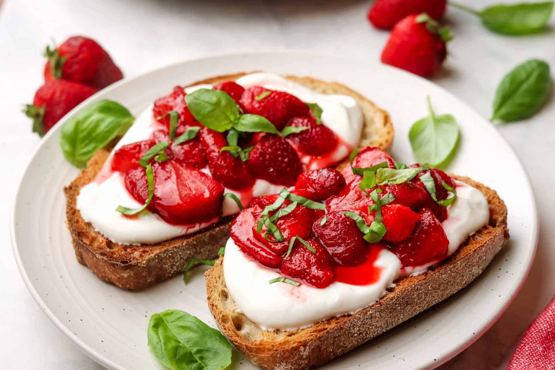 two pieces of toast on a plate with whipped ricotta and strawberries on top garnished with fresh basil