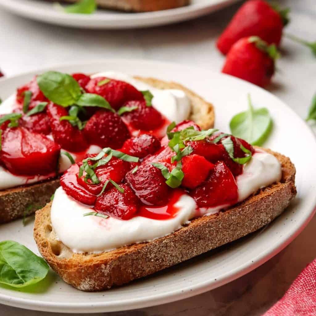 Strawberry ricotta toast garnished with basil on a plate.