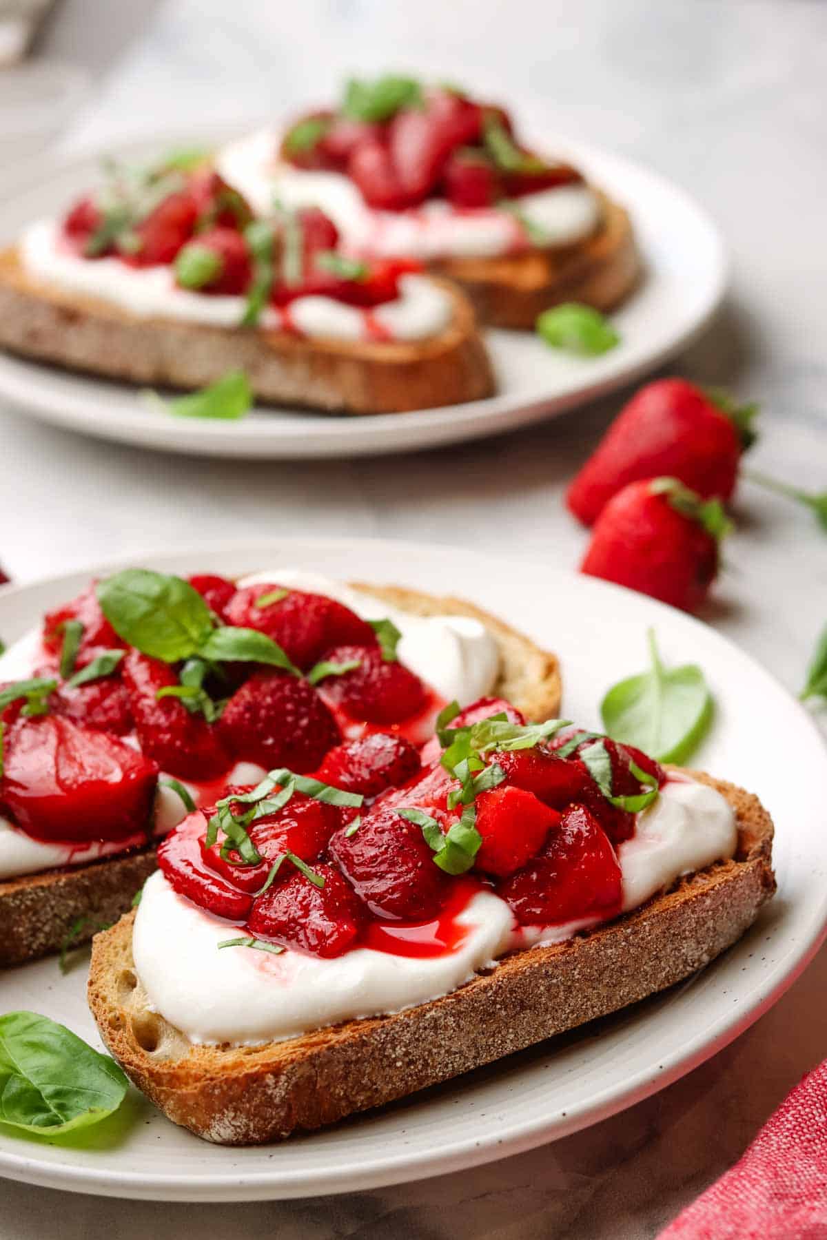 two pieces of toast on a plate with whipped ricotta and strawberries on top garnished with fresh basil.