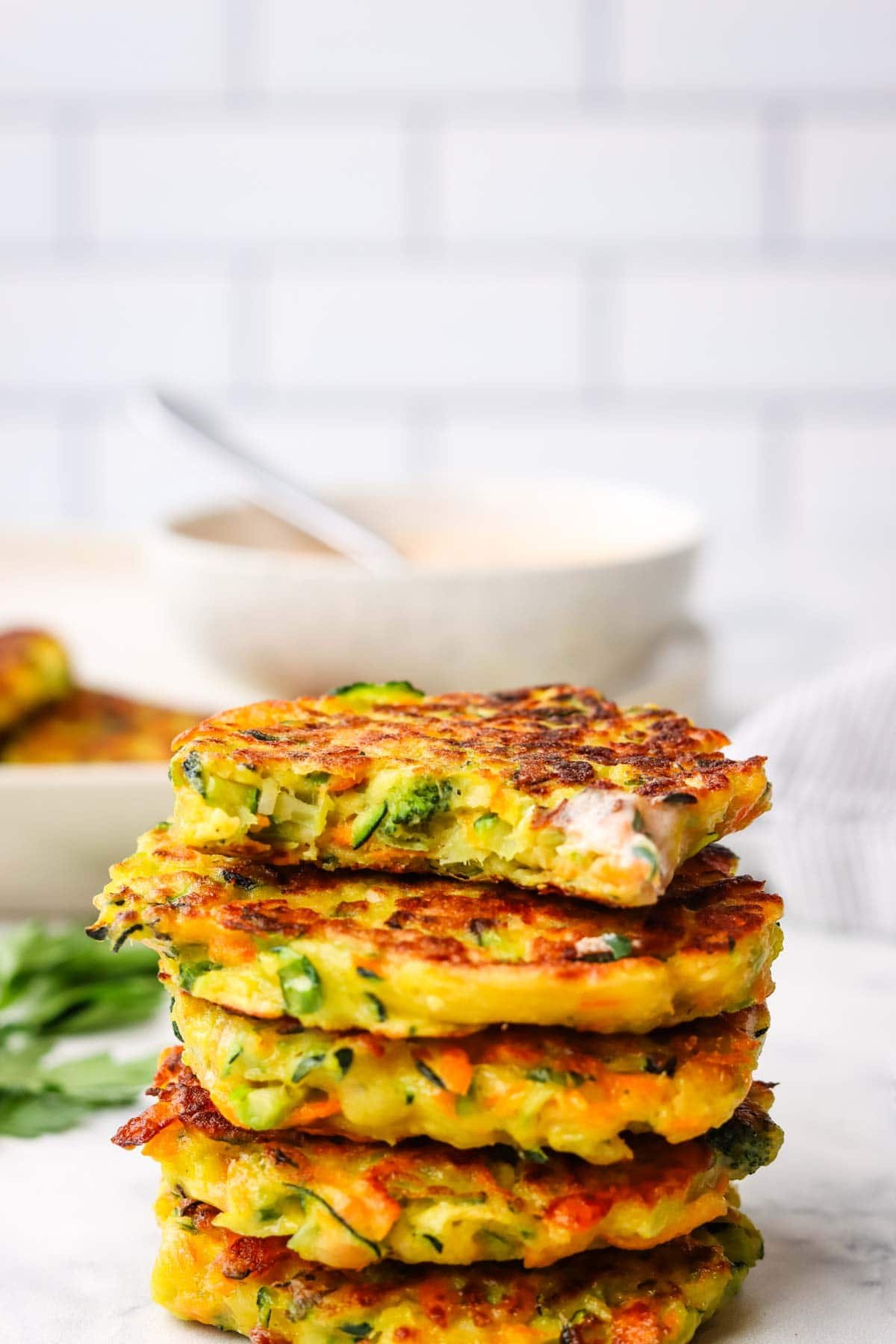 a stack of vegetable fritters stacked on a plate with a bite taken out from the top fritter