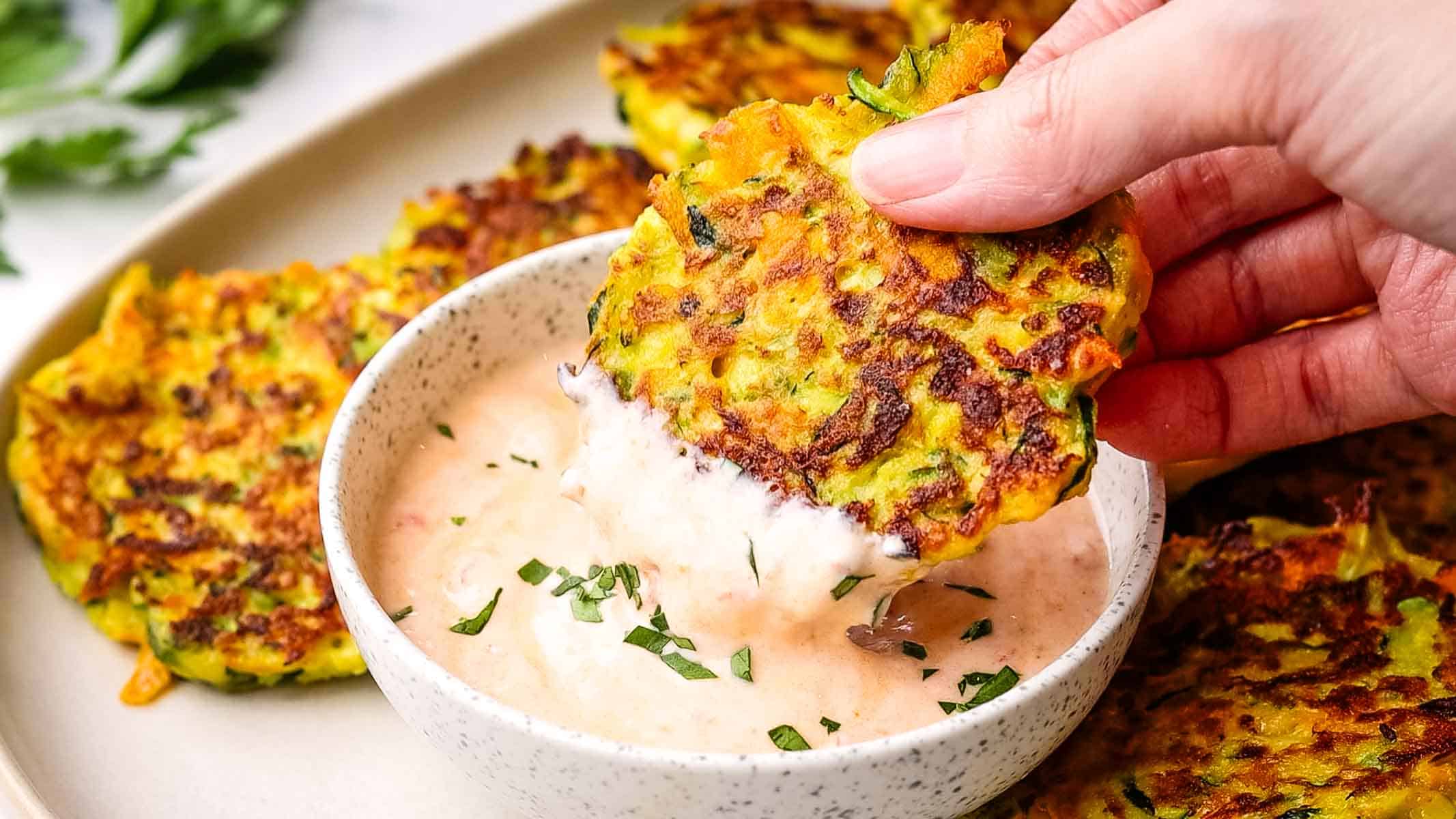 a hand dipping a fritter in sauce
