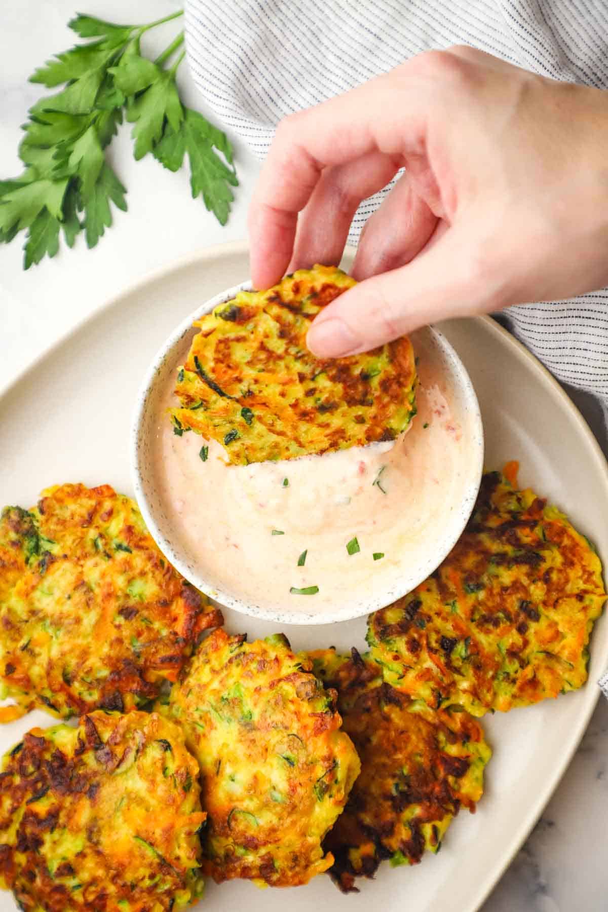 a hand dipping a vegetable fritter in a dipping sauce
