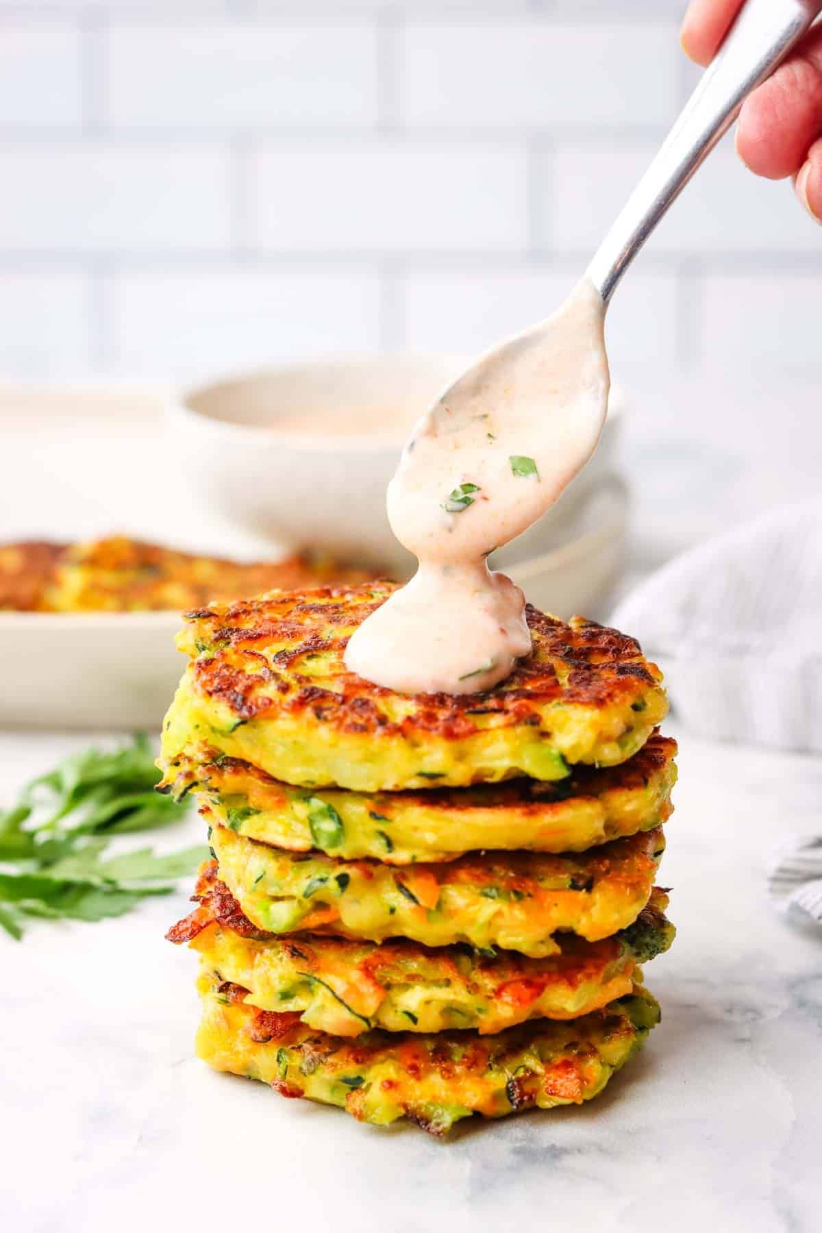 spooning dipping sauce on a stack of vegetable fritters