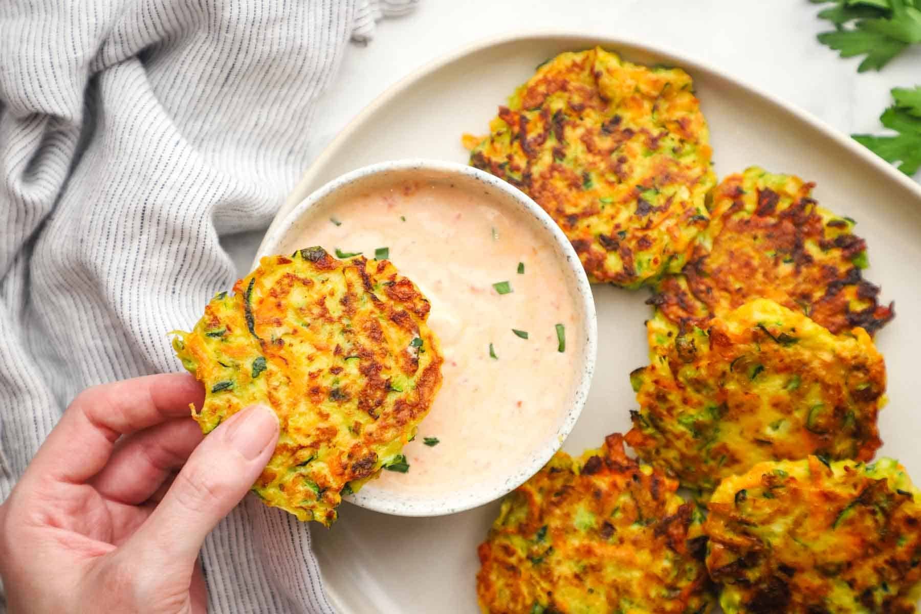 a hand dipping a vegetable fritter in a dipping sauce