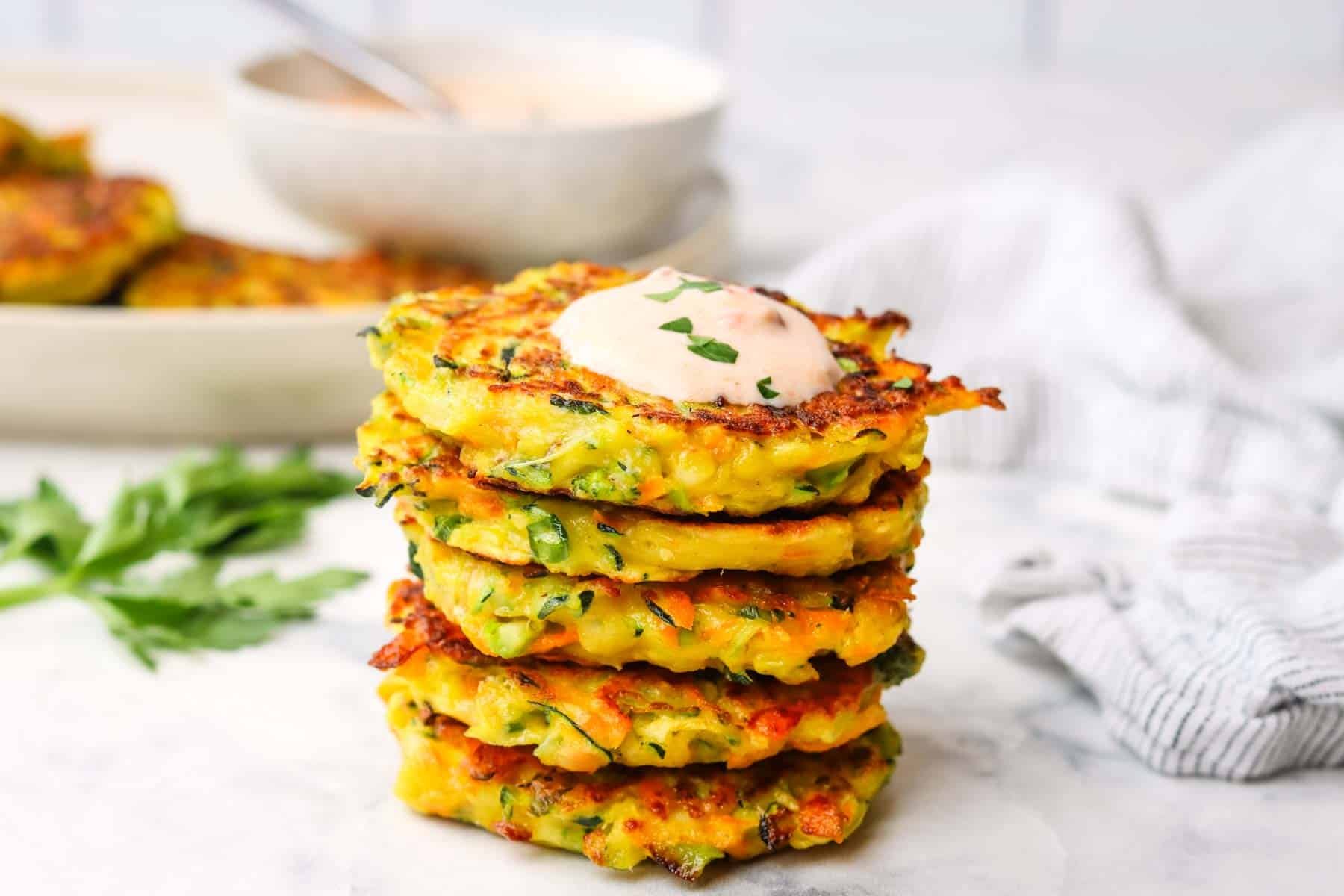 A stack of vegetable fritters with a dollop of dip on top.