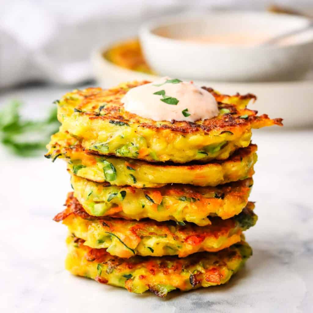 a stack of vegetable fritters topped with a dipping sauce